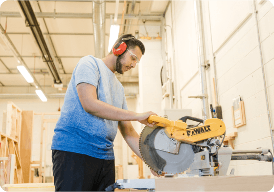 Construction student in workshop using machinery wearing goggles and ear defenders